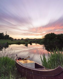 Boats moored on river against sky at sunset