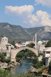 Arch bridge over river amidst buildings in city against sky