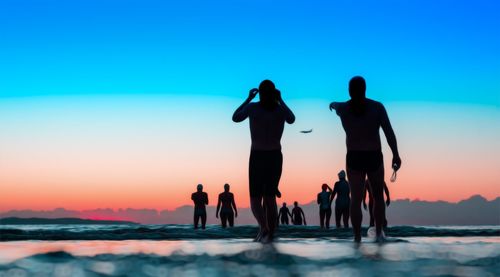 Silhouette people at beach against sky during sunset