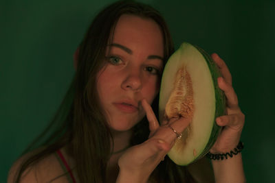 Portrait of young woman holding melon against wall