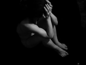 Midsection of shirtless man sitting against black background