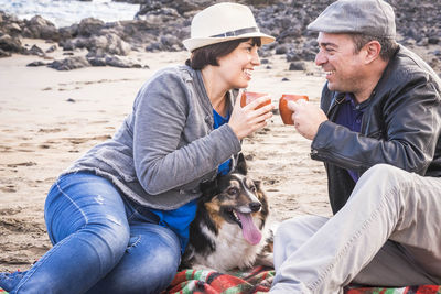 Couple having tea with dog on shore at beach