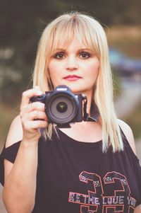 Portrait of beautiful woman holding camera outdoors