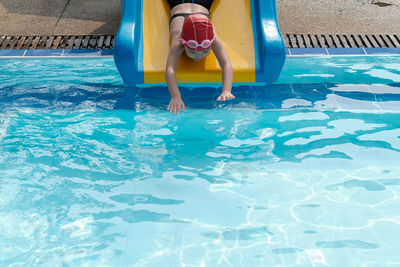 Playful girl sliding from water slide in swimming pool