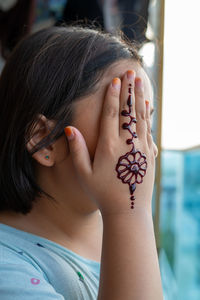 Portrait of henna ornaments on young girl's hand covering face.