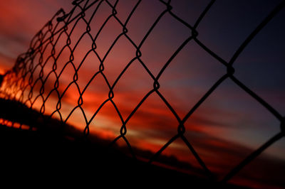 Close-up of silhouette chainlink fence against sky during sunset