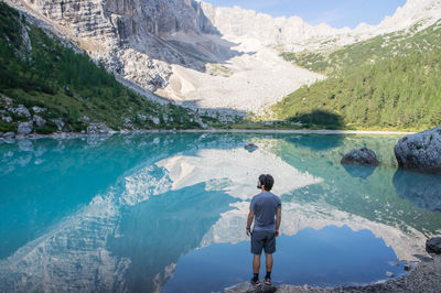 Rear view of man standing by lake against mountain