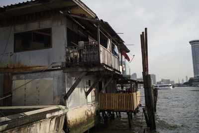 Abandoned building by river in city against sky