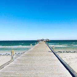 Pier over sea against clear blue sky