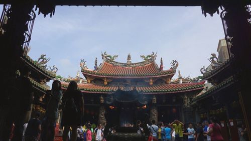 Low angle view of people outside temple against sky