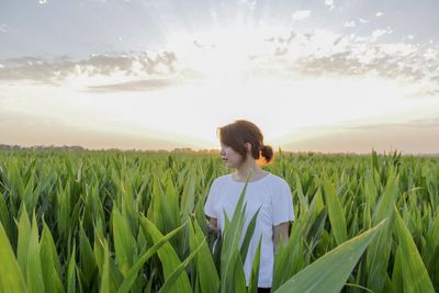 Woman standing on field amidst plants against cloudy sky