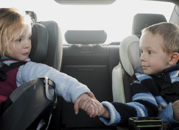 Siblings holding hands while sitting in car