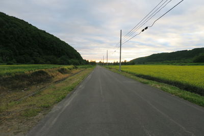 Country road amidst field against sky