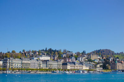 Buildings by sea against clear blue sky