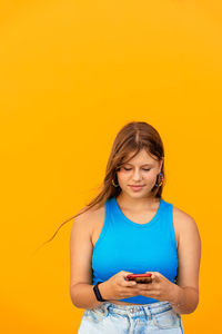 Teenager girl in blue top using smartphone texting friends or scrolling media at yellow background