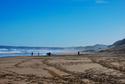 People at beach against clear blue sky