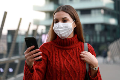 Young woman wearing mask using mobile phone outdoors