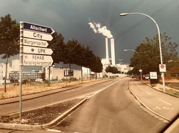 Road sign by street in city against sky