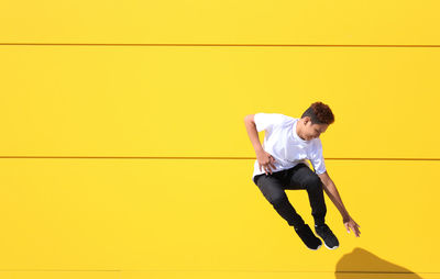 Full length of teenage boy jumping by yellow wall