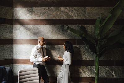Businessman and businesswoman leaning on wall while discussing strategy together at law office