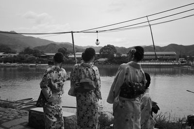 Women in kimono standing at lakeshore against sky