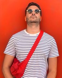 Portrait of man wearing sunglasses while standing against red background