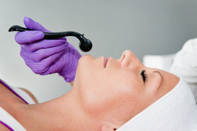 Close-up of woman lying down with while beautician using cosmetic roller on face at spa