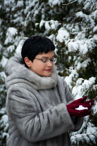 Woman in a gray fur coat with red gloves holds snow in her hands. 