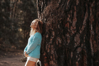 Young woman standing by tree trunk