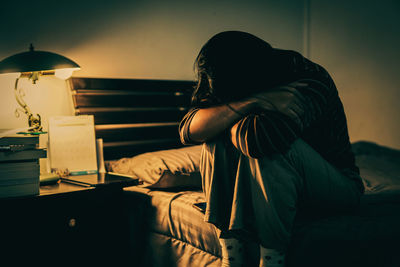 Woman using phone while sitting on bed at home