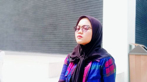 Portrait of young woman standing against wall