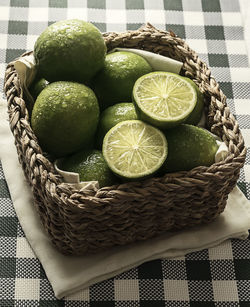 High angle view of wet limes in basket on tablecloth