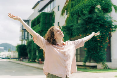 Young woman with arms raised standing against sky