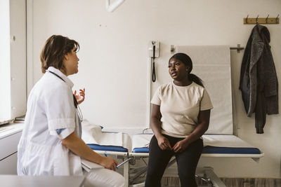 Female medical expert discussing with patient sitting on examination table at medical clinic