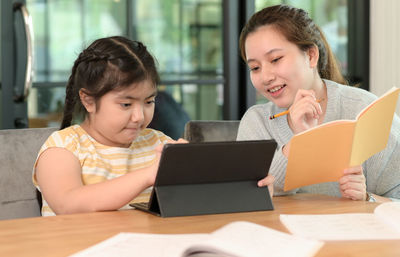 Asian girl studying privately with tutor at home, siblings teaching homework, online learning.