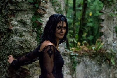 Side view of young woman standing against tree trunk