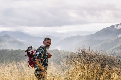 Front view of traveler looking at camera with his dog in backpack in the mountains