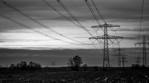 Electricity pylon on field against cloudy sky