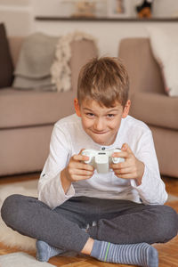 Portrait of boy holding video game remote control in living room at home 