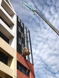 Low angle view of crane by building against sky