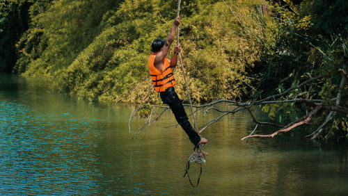 Side view full length of man swinging on rope over lake at forest