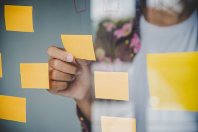 Midsection of businesswoman holding adhesive note on glass