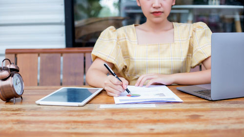 Midsection of woman using mobile phone while sitting on table