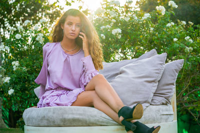 Beautiful young woman sitting on sofa against plants