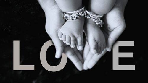 Cropped hands holding feet of baby against love text on black background
