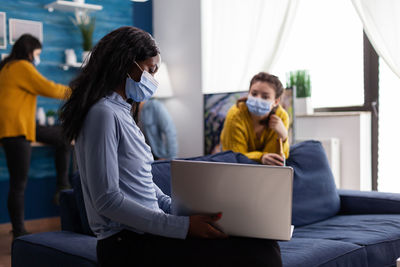 Woman wearing mask using laptop at home