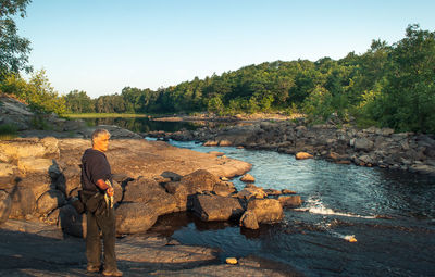 Rear view of man standing by river against clear sky