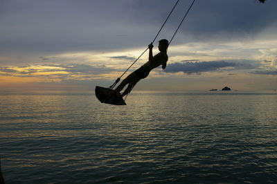 Silhouette of woman jumping in sea at sunset