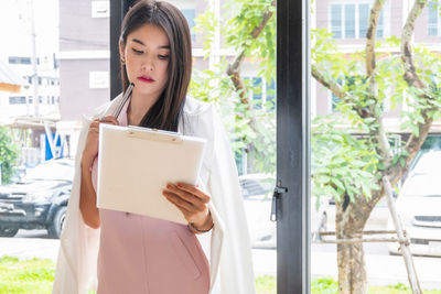 Woman looking at camera while standing by window