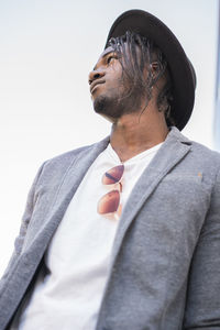 Low angle view of young man with braided hair wearing hat against clear sky